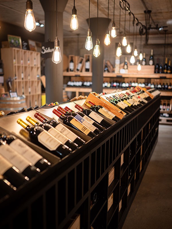 Lange Reihen von Weinflaschen liegen schräg in Regalen in einem Verkaufsraum mit Hängelampen.