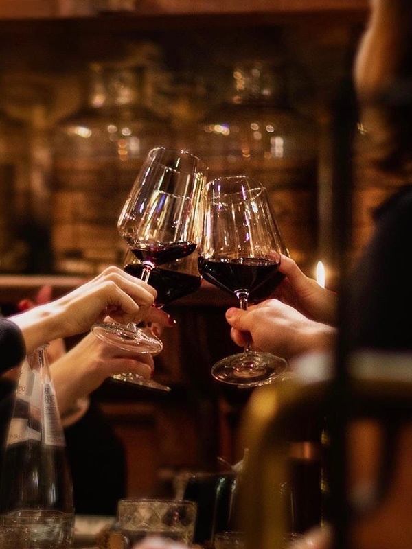 Mehrere Hände stoßen mit halb-gefüllten Rotweingläsern in einem gemütlichen Restaurant an