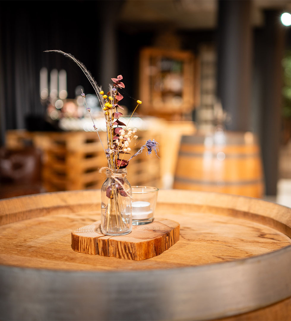 Glasvase mit getrockneten Blumen auf einem runden Holztisch im Weinkeller des Wyhus Belp