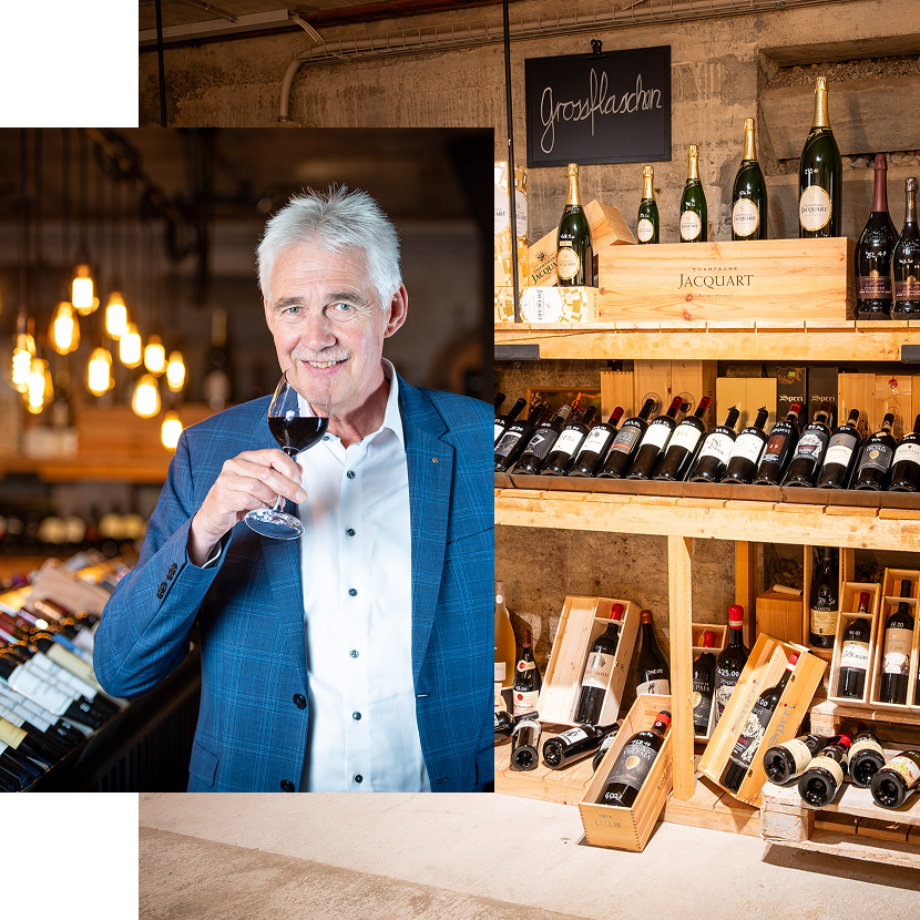 Daniel Ingold, Geschäftsführer von Wyhus Belp, steht vor gefüllten Weinregalen im Weinkeller der Vinothek und trinkt Rotwein