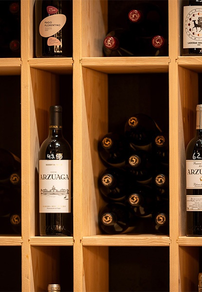 Weinflaschen in einem hölzernen Weinregal, teilweise mit sichtbaren Etiketten, in warmem Licht.